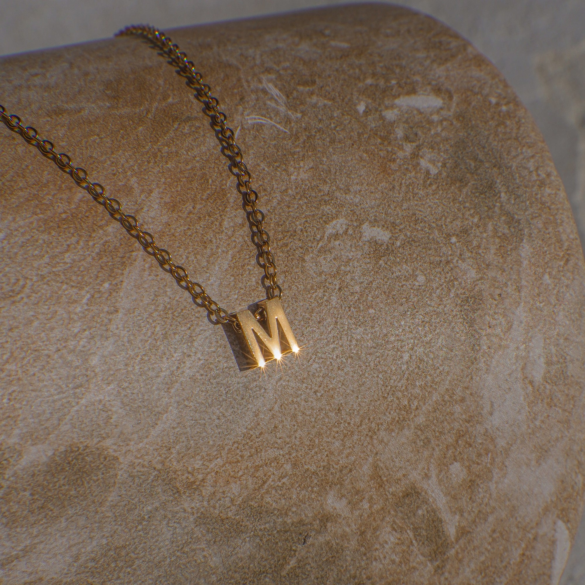 Gold necklace with a 'M' pendant on a textured stone surface