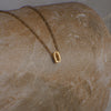 Gold necklace with a letter 'O' pendant on a stone surface