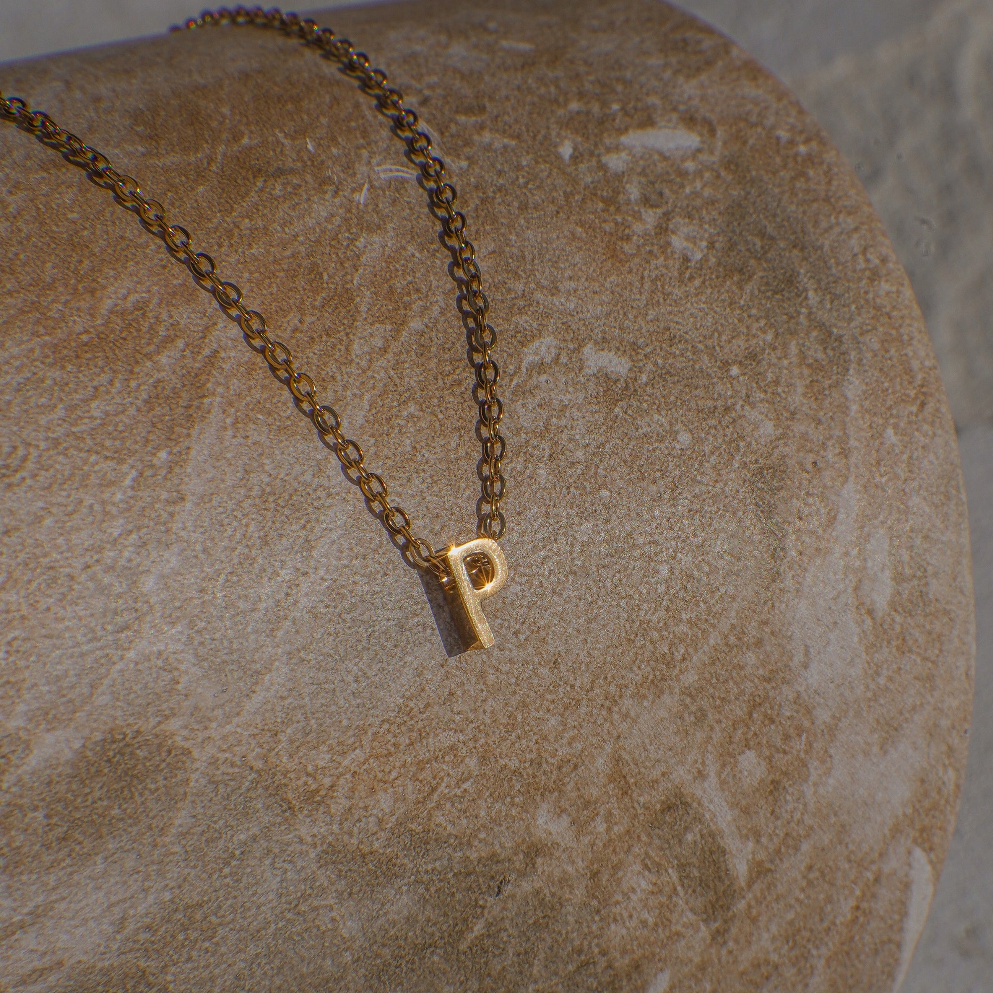 Gold necklace with a 'P' pendant on a textured stone surface