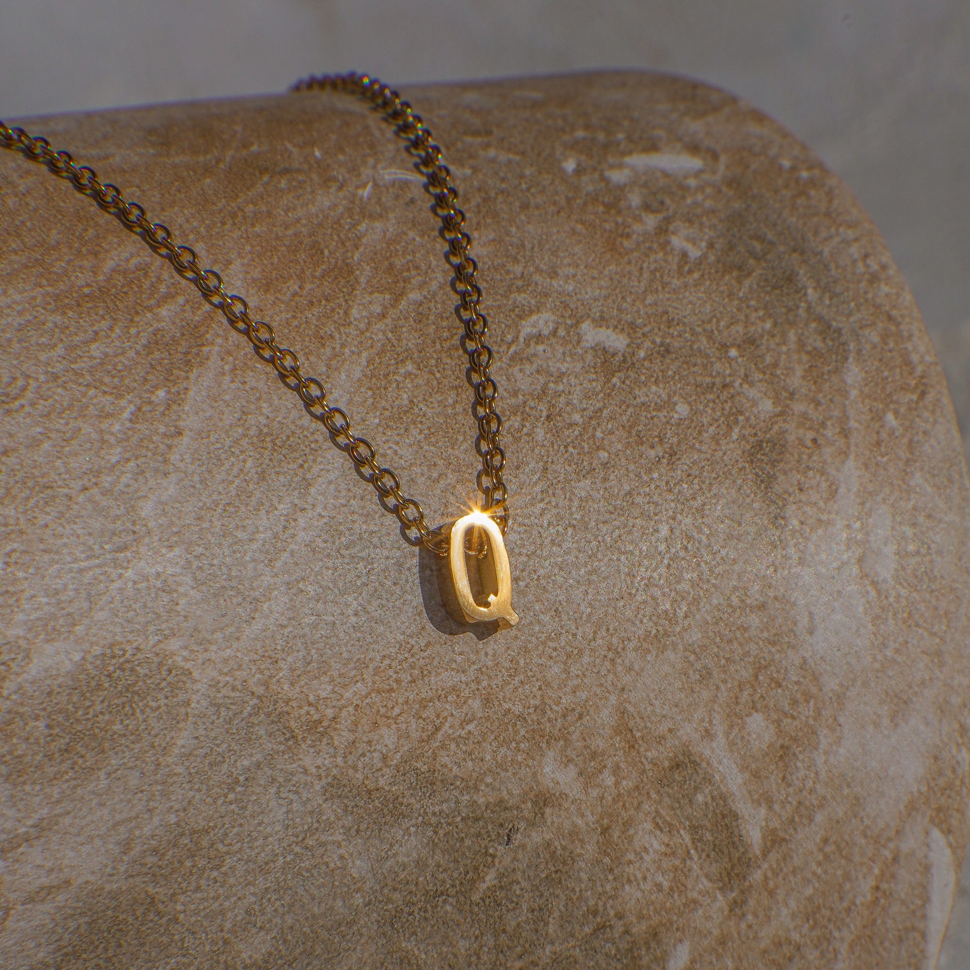 Gold necklace with a letter 'Q' pendant on a stone surface