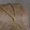 Gold necklace with a 'S' pendant on a stone surface