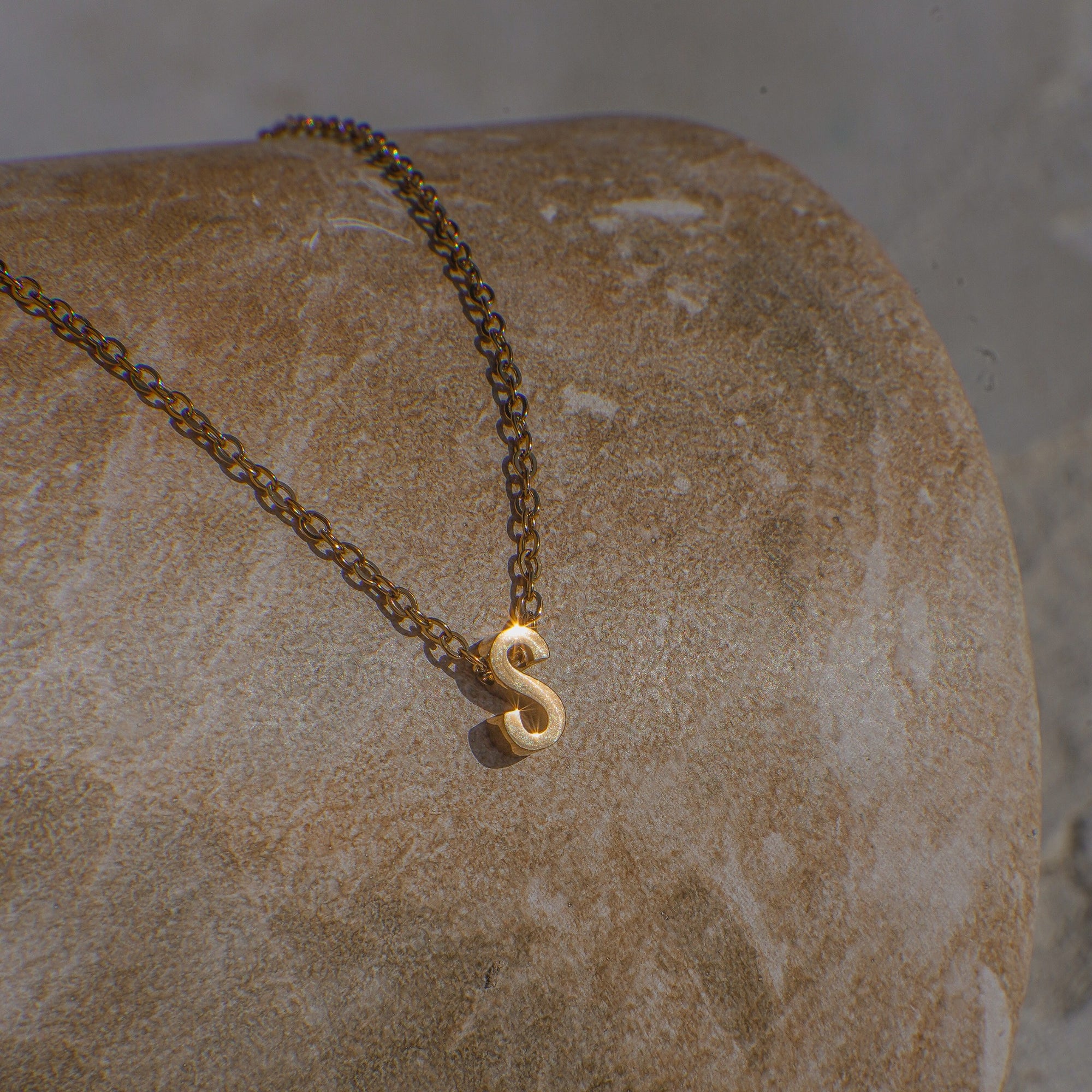 Gold necklace with a 'S' pendant on a stone surface