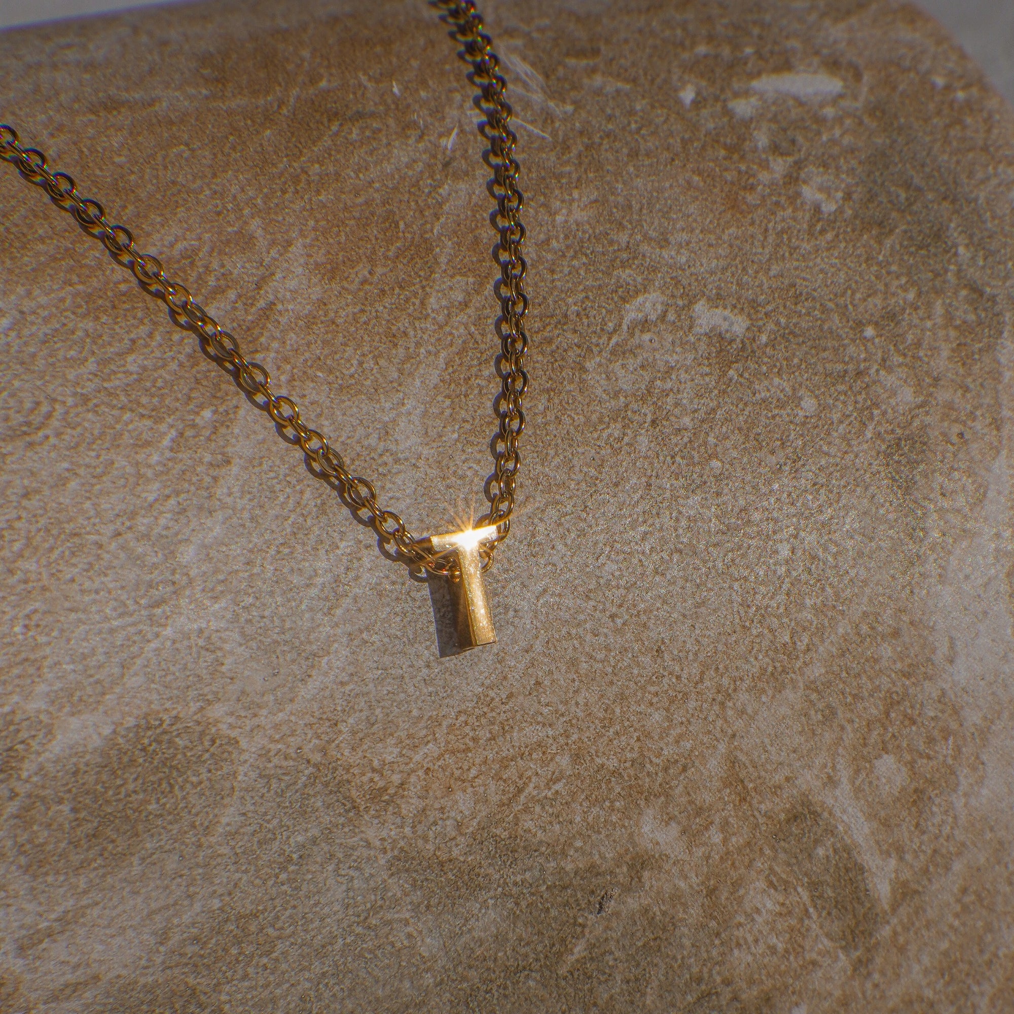 Gold necklace with letter 'T' pendant on a textured beige surface