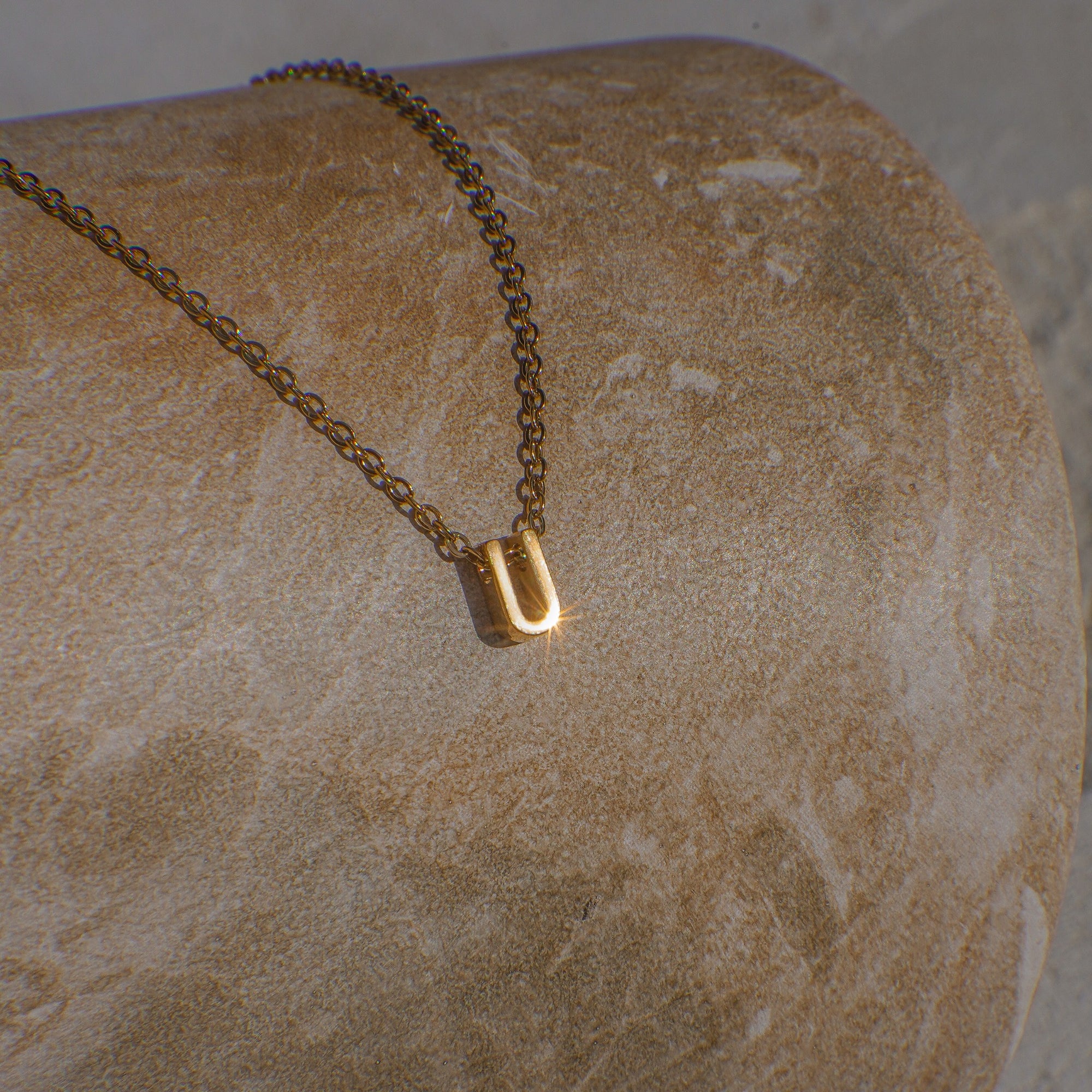 Gold necklace with a 'U' pendant on a textured stone surface