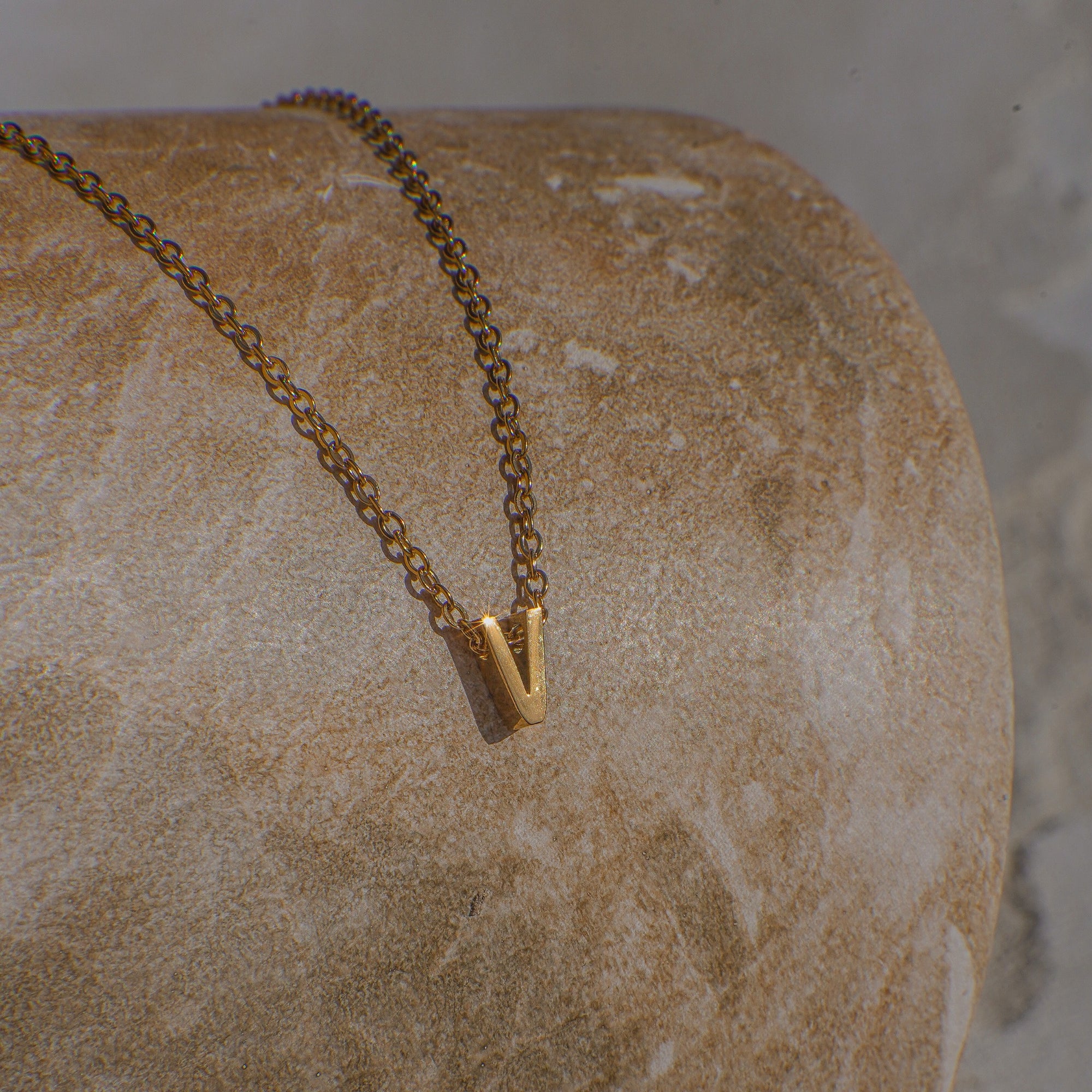 Gold necklace with a 'V' pendant on a textured stone surface