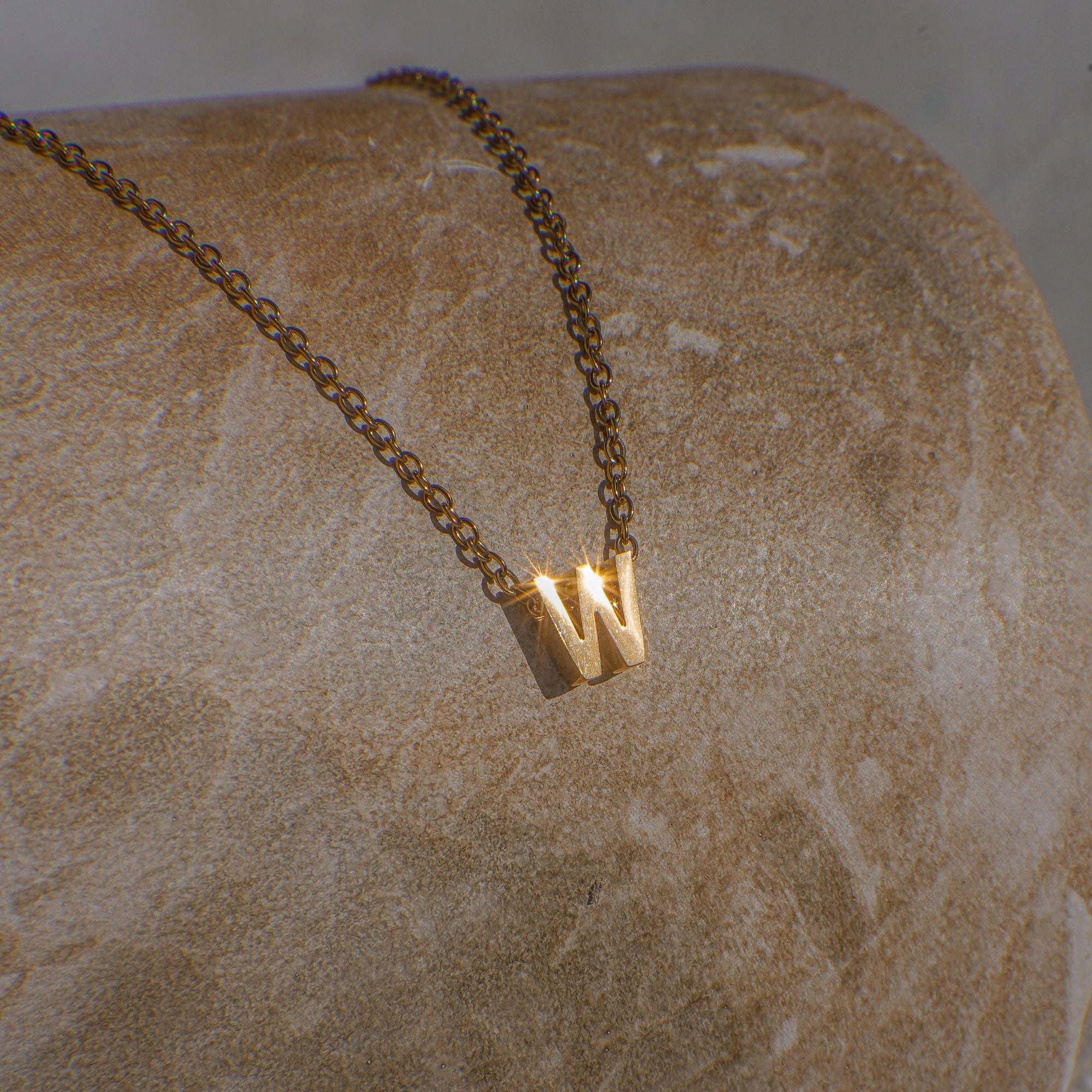 Gold necklace with a 'W' pendant on a textured stone surface