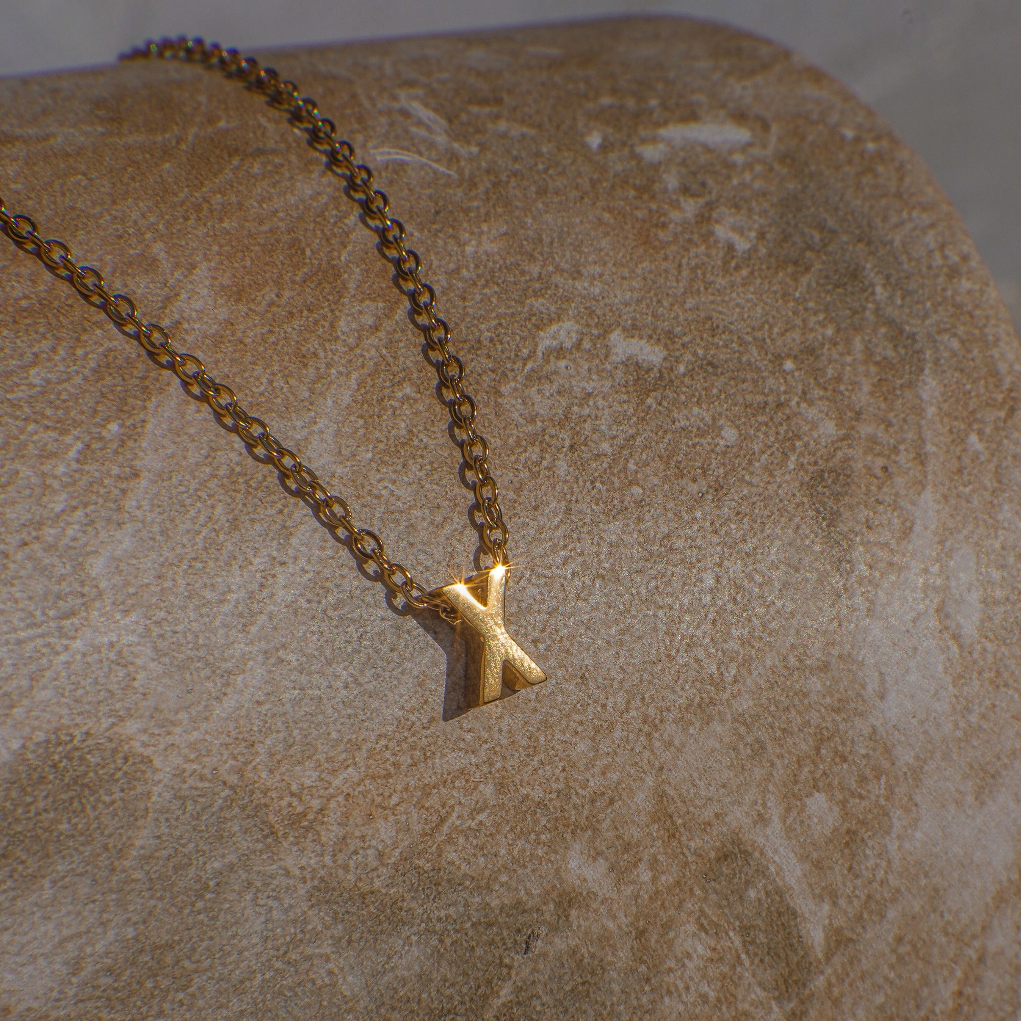 Gold necklace with a 'X' pendant on a textured beige surface