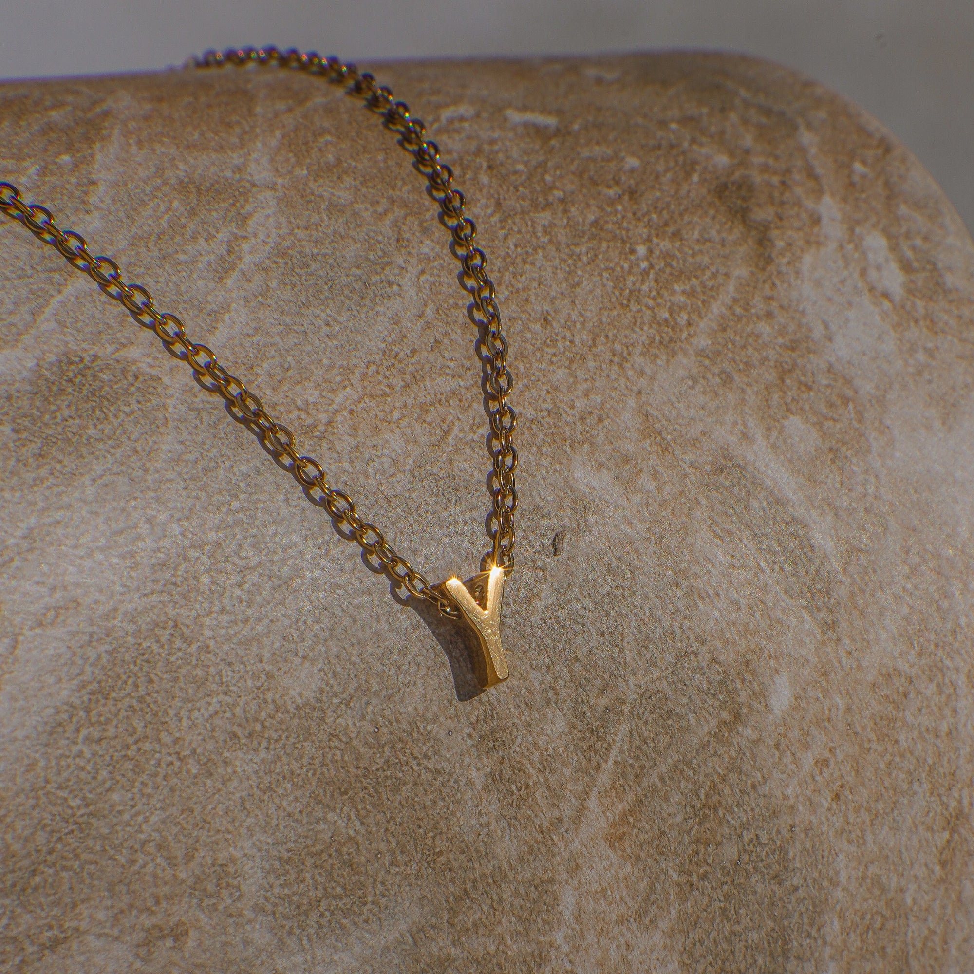 Gold necklace with a 'Y' pendant on a textured beige surface