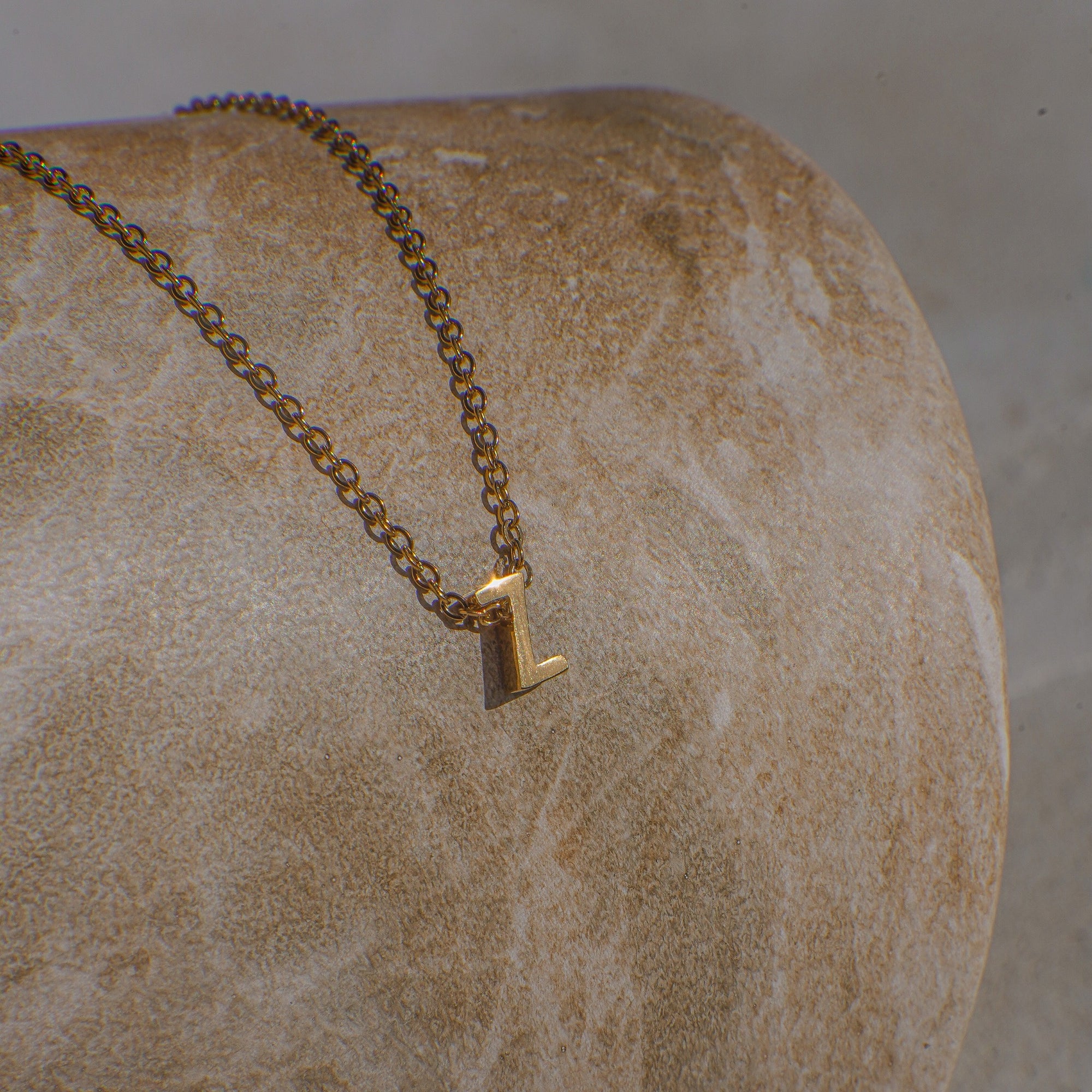 Gold necklace with a letter 'Z' pendant on a stone surface