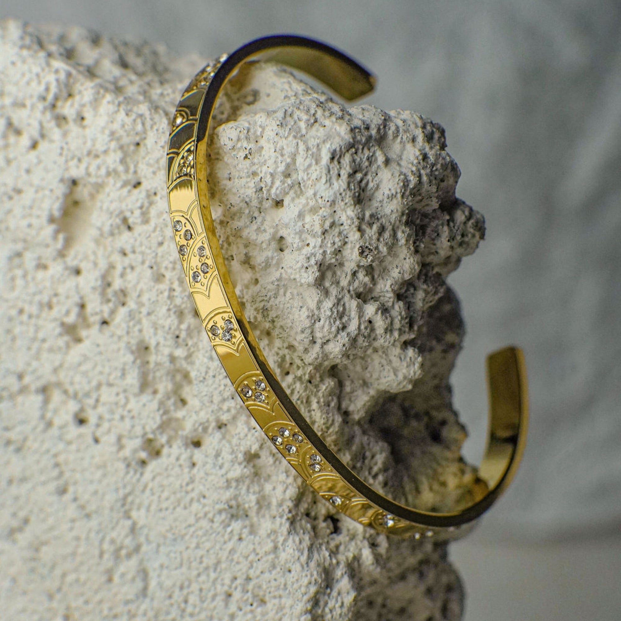 Gold bracelet with intricate designs on a textured stone surface