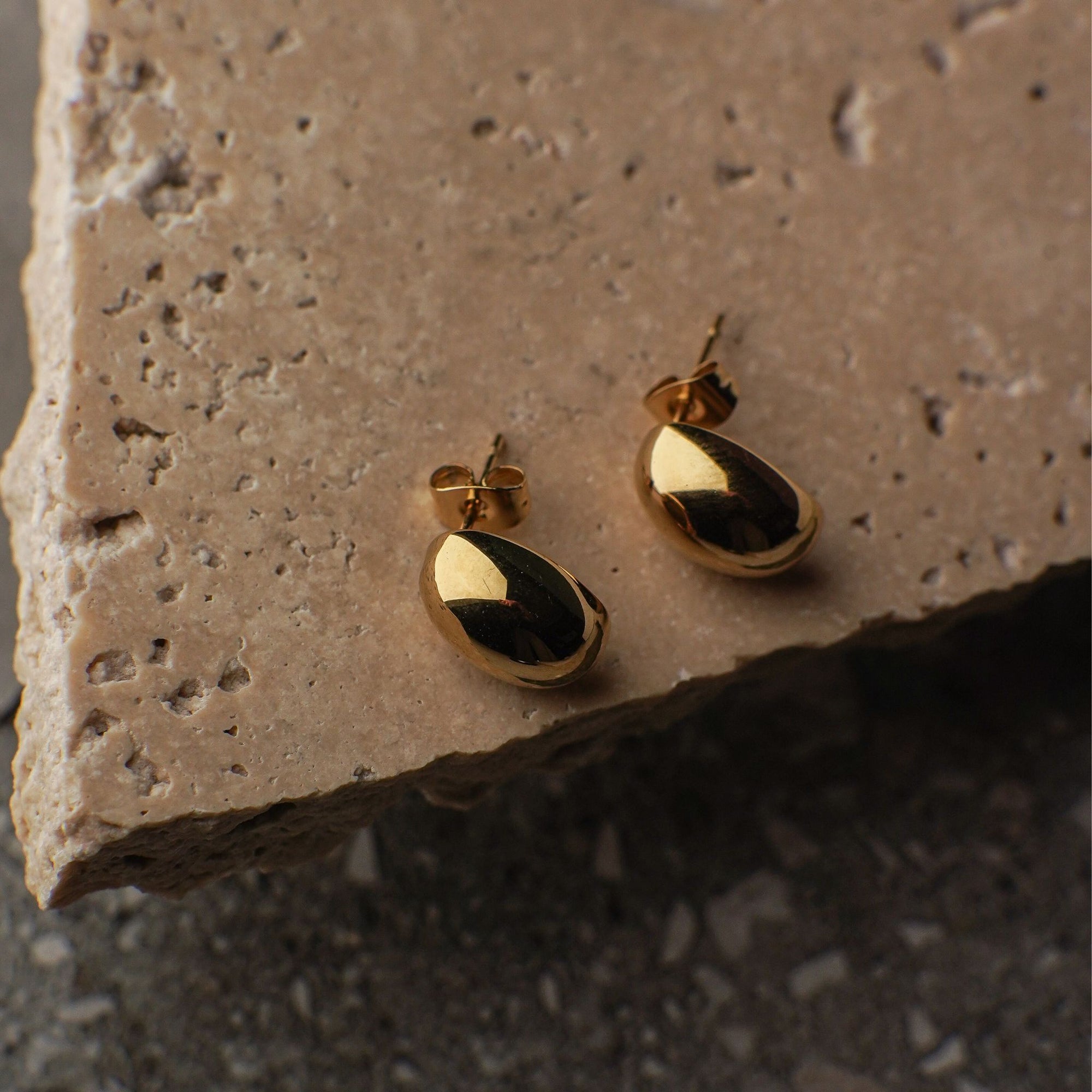 Gold earrings on a textured stone surface