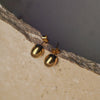 Gold earrings on a textured stone surface with a blurred background
