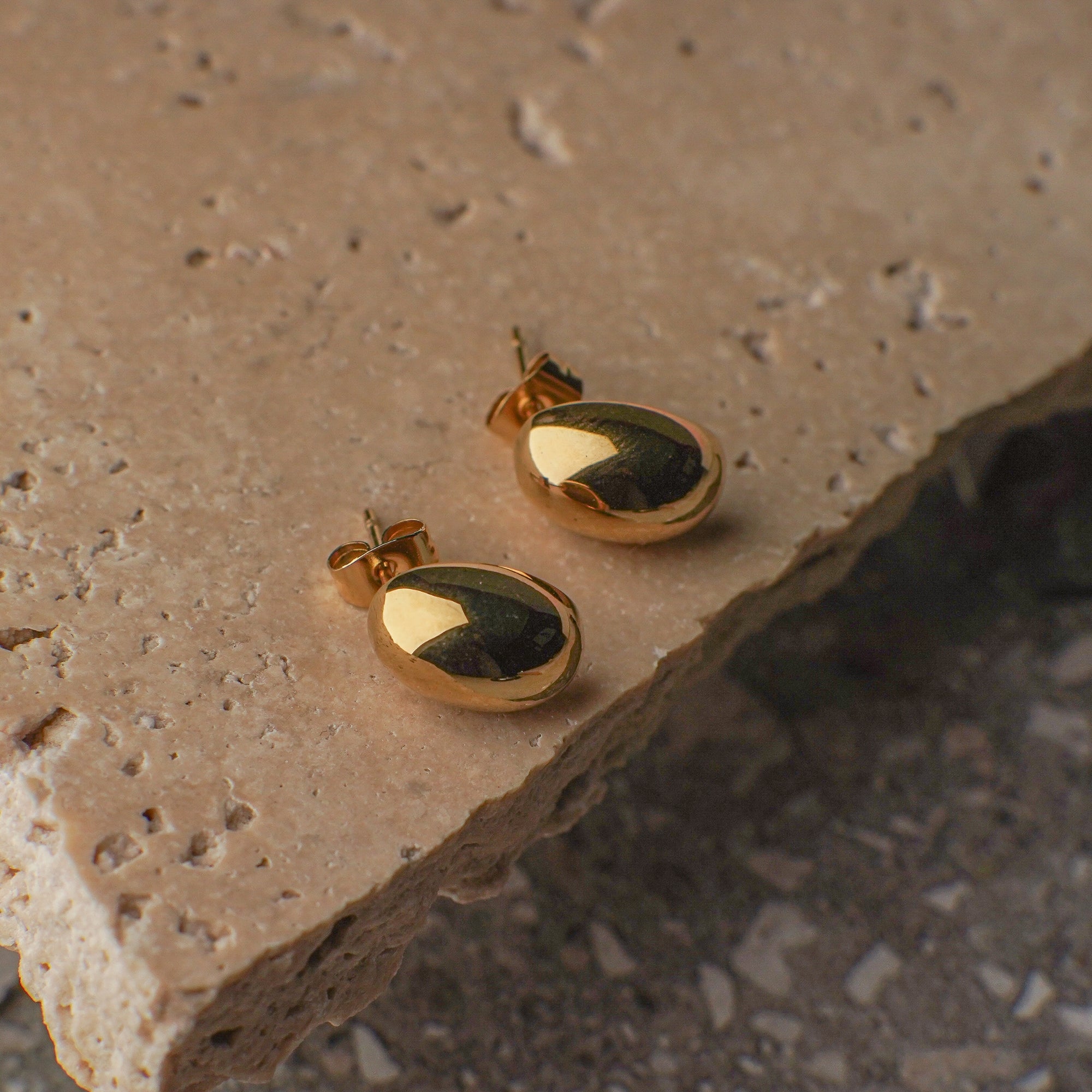 Gold earrings with a green stone on a textured stone surface