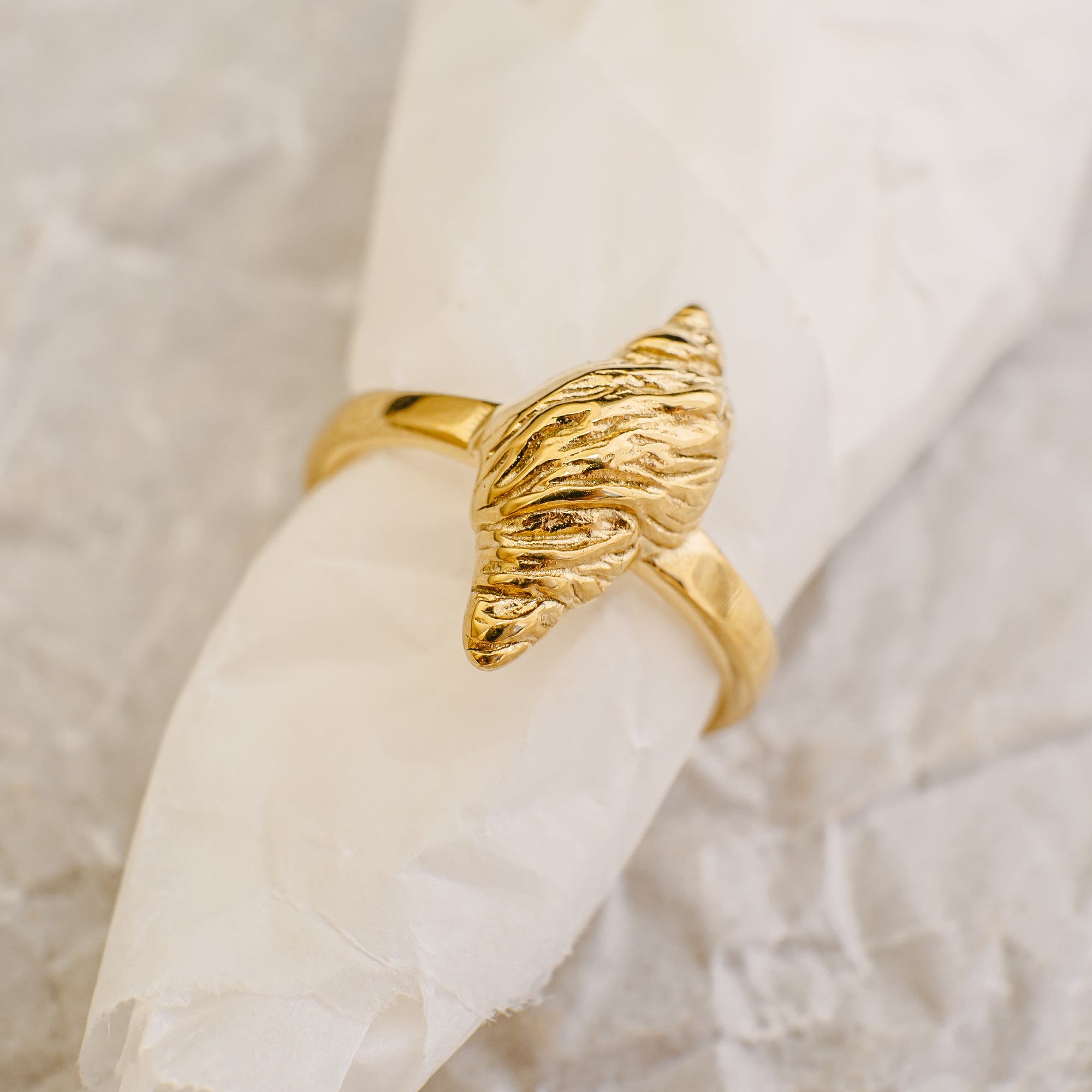 Gold leaf-shaped ring on a white fabric background