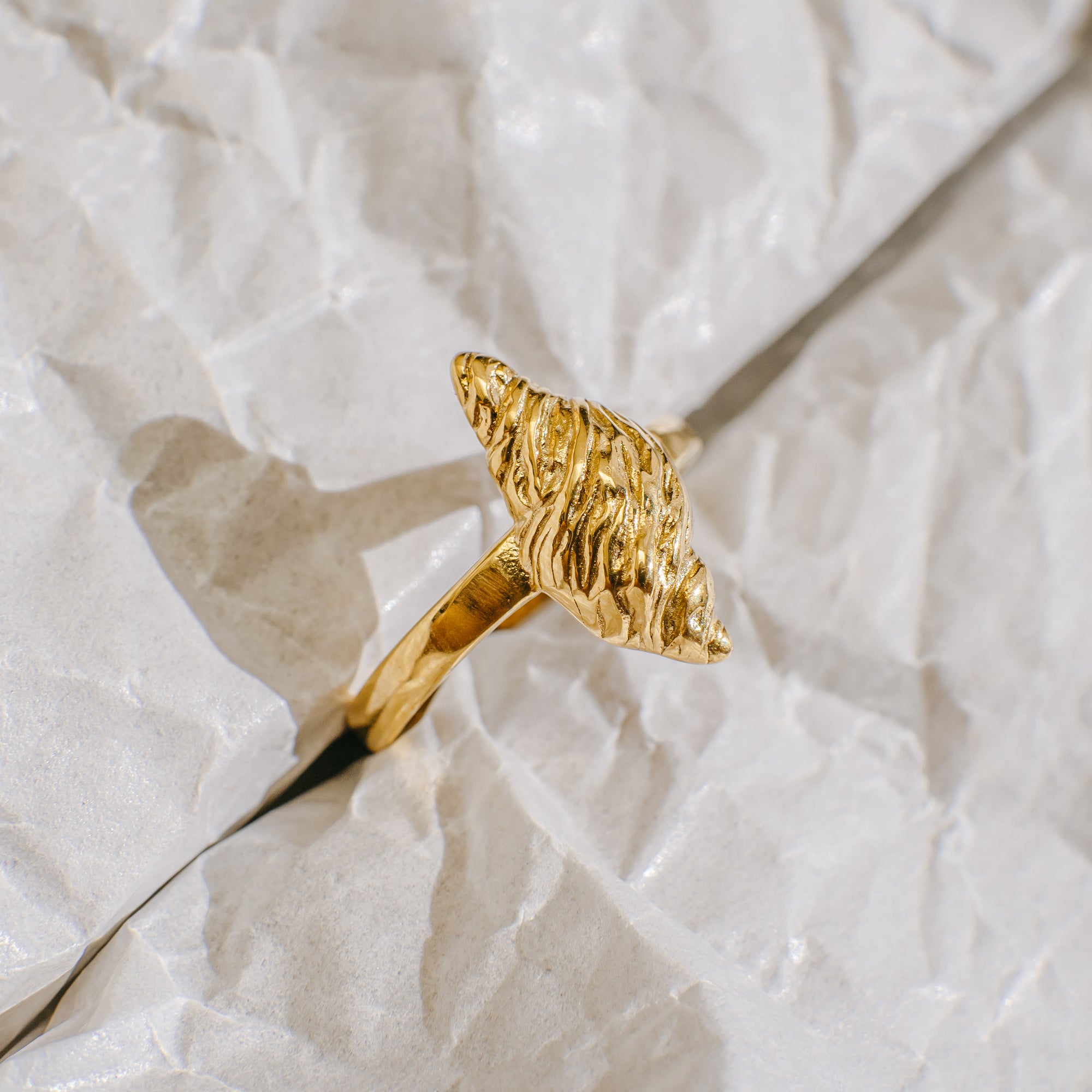 Gold ring with a textured design on a light beige fabric background