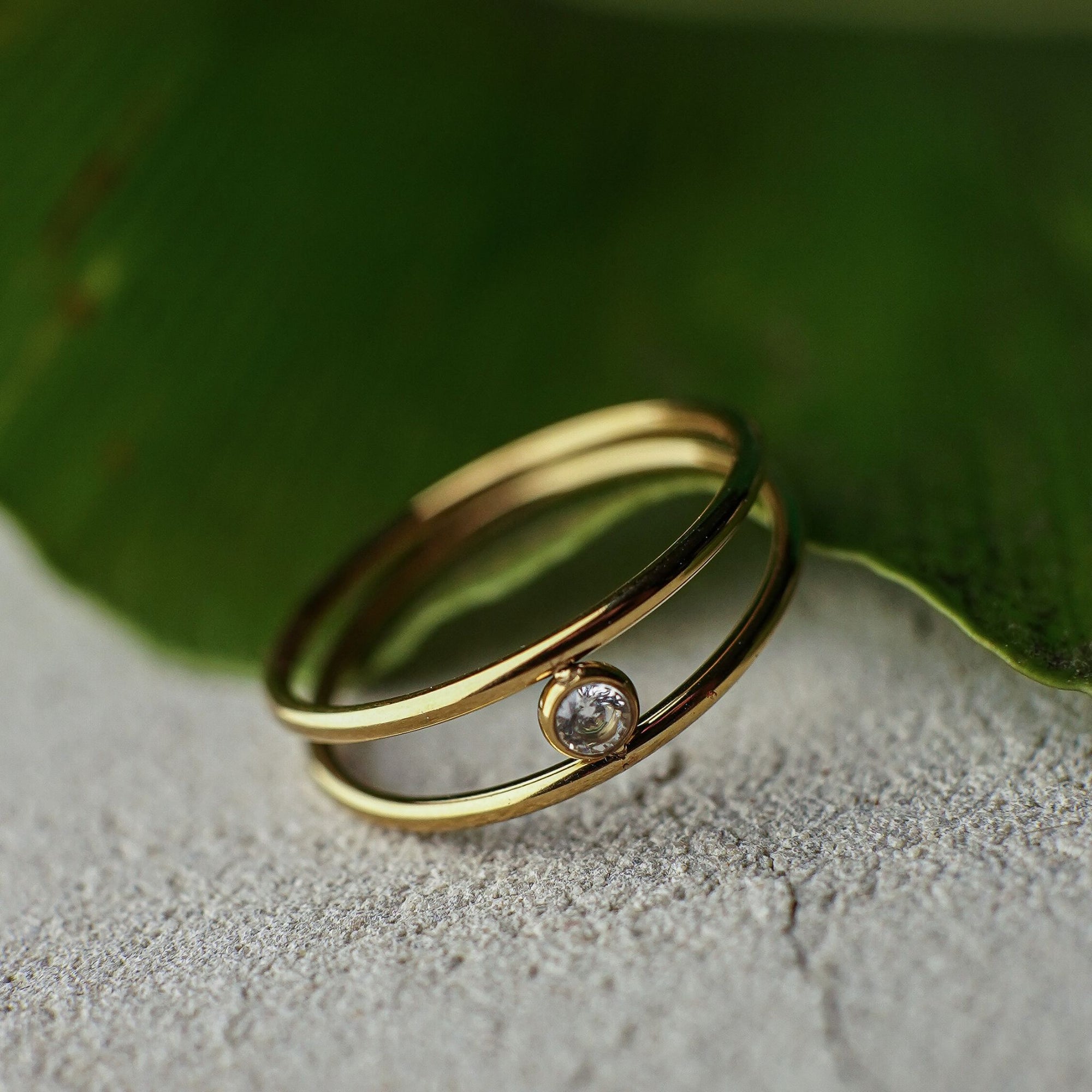 Gold ring with a diamond on a textured surface with a green leaf background