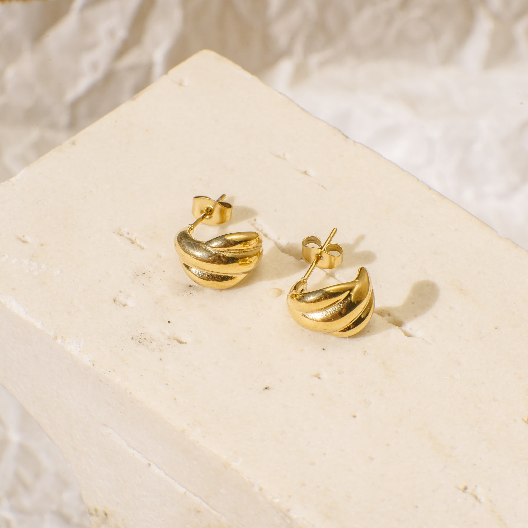 Gold earrings on a beige stone surface