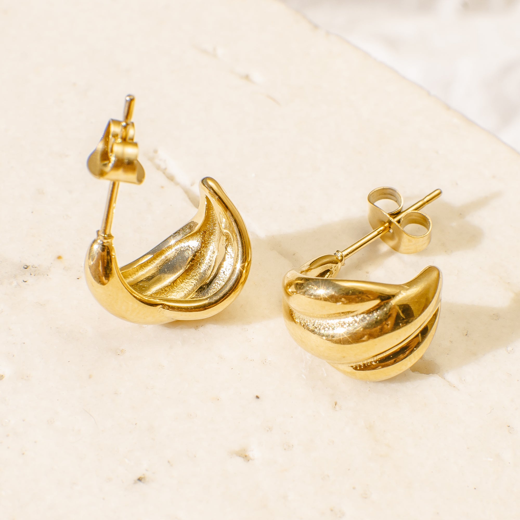 Gold earrings on a textured beige surface