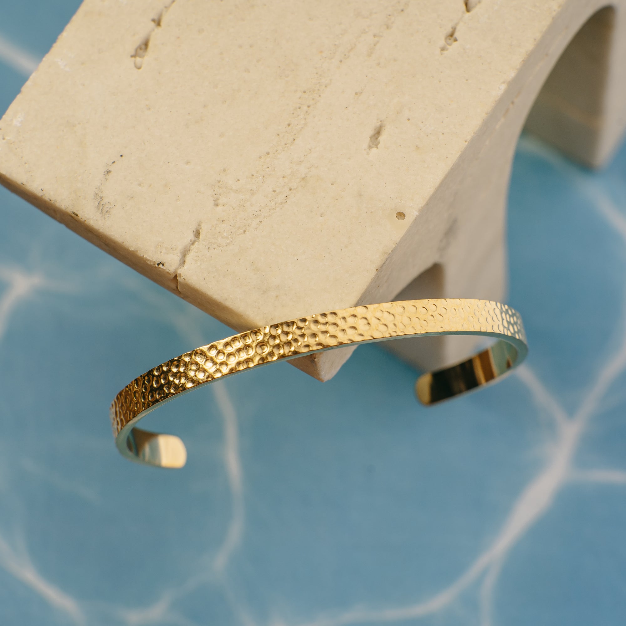Gold bracelet on a white stand with a blue textured background