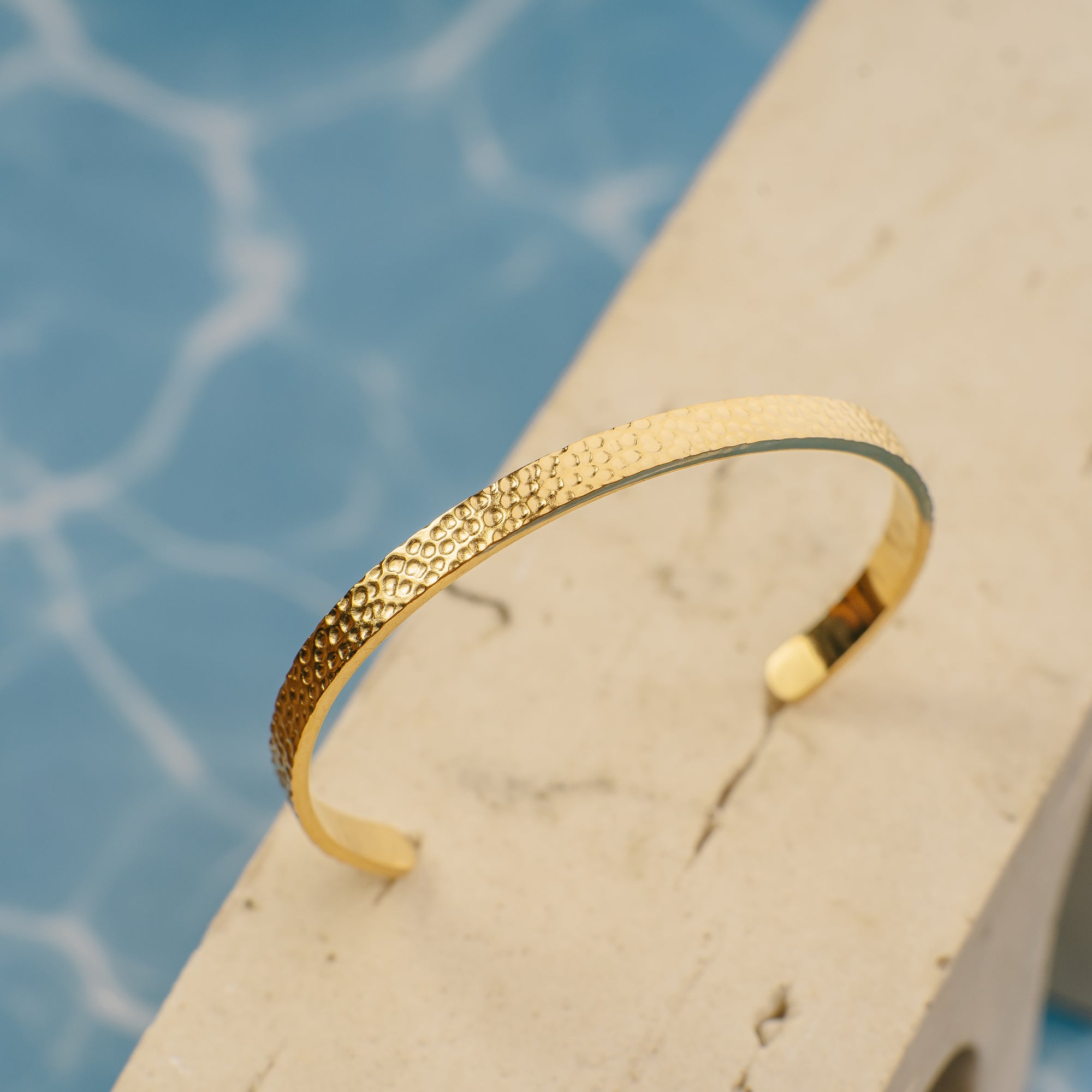 Gold bracelet on a stone surface with water in the background