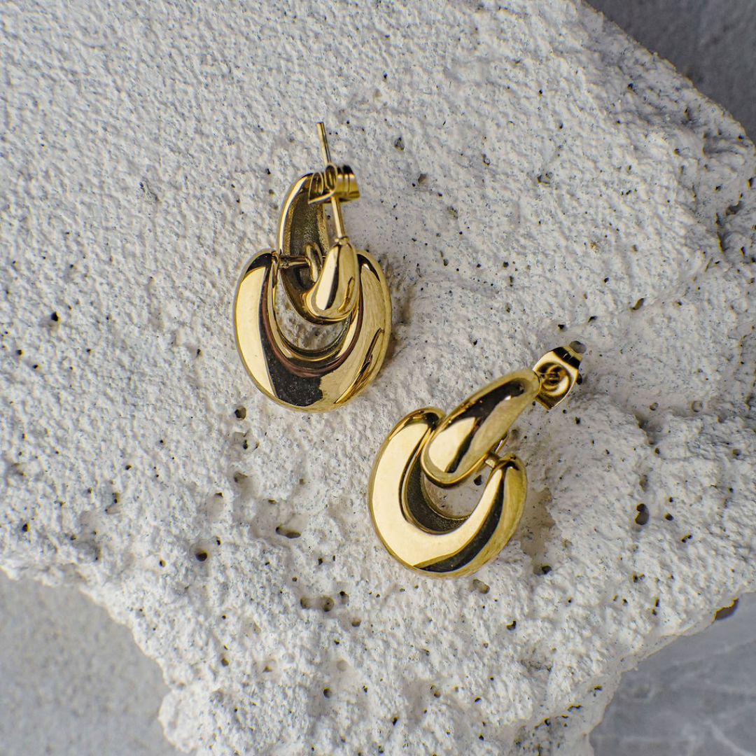 Gold hoop earrings on a textured stone surface