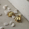 Gold shell-shaped earrings on a textured surface with small stones.
