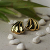 Gold and black shell-shaped earrings on a textured surface with stones and leaves.