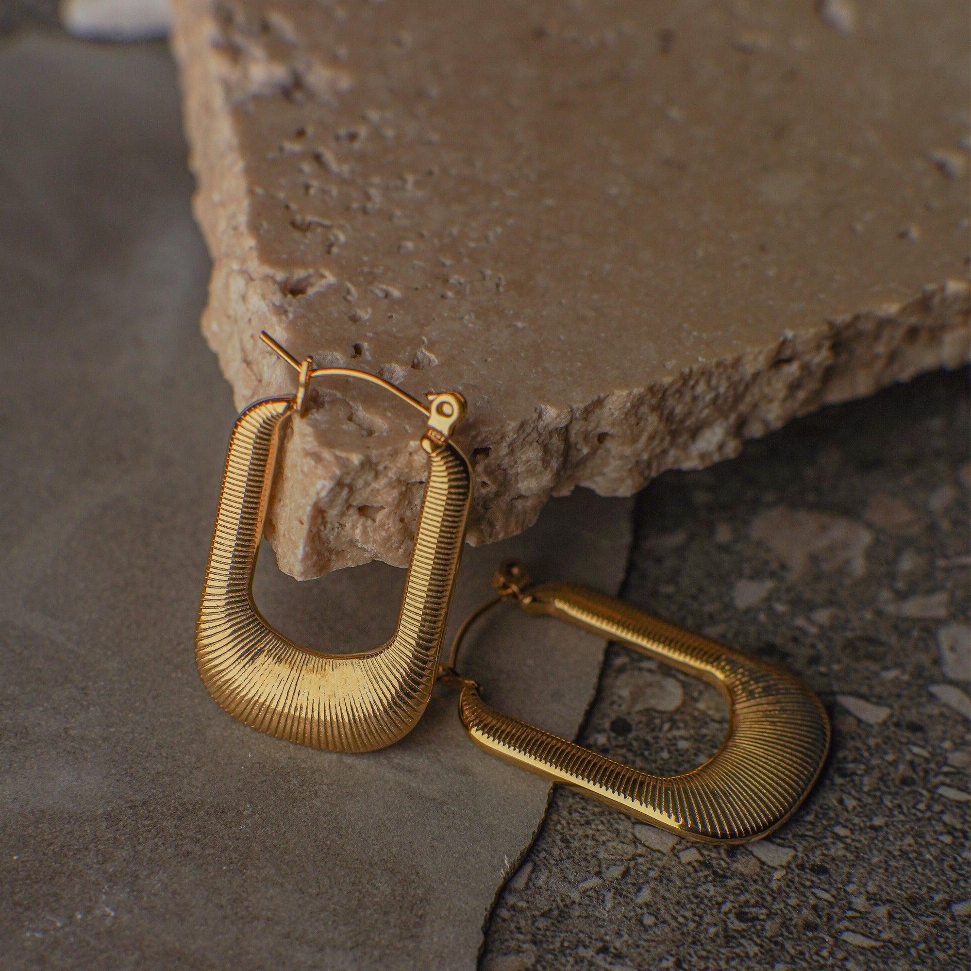 Gold hoop earrings on a stone surface