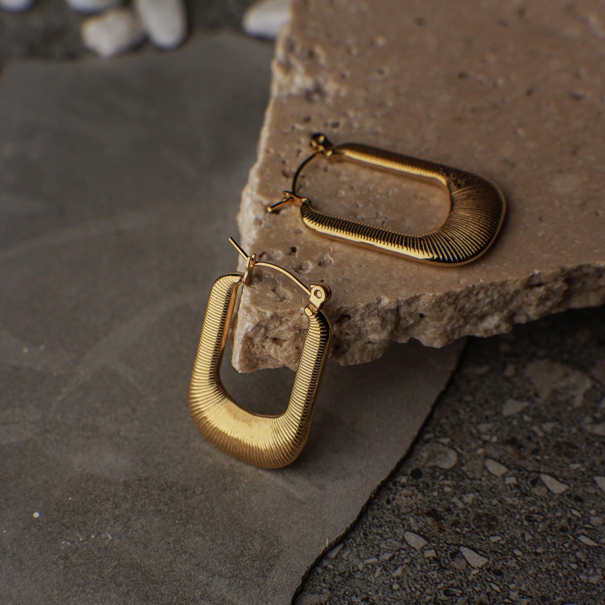 Gold hoop earrings on a textured stone surface