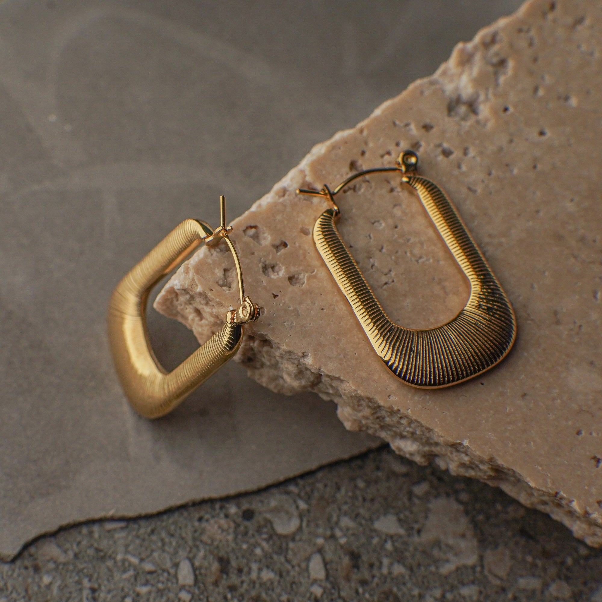 Gold hoop earrings on a textured stone surface