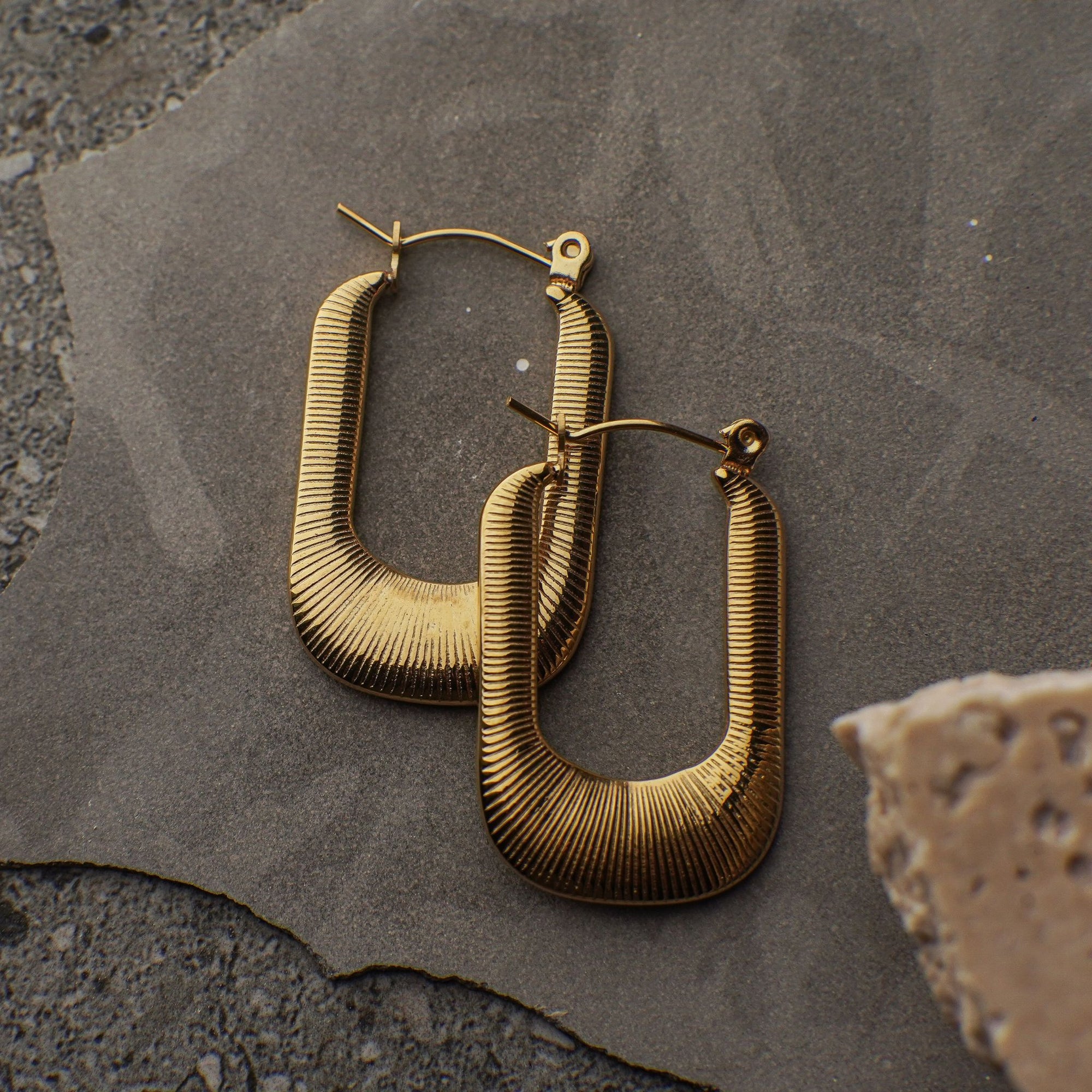 Gold hoop earrings on a textured stone surface