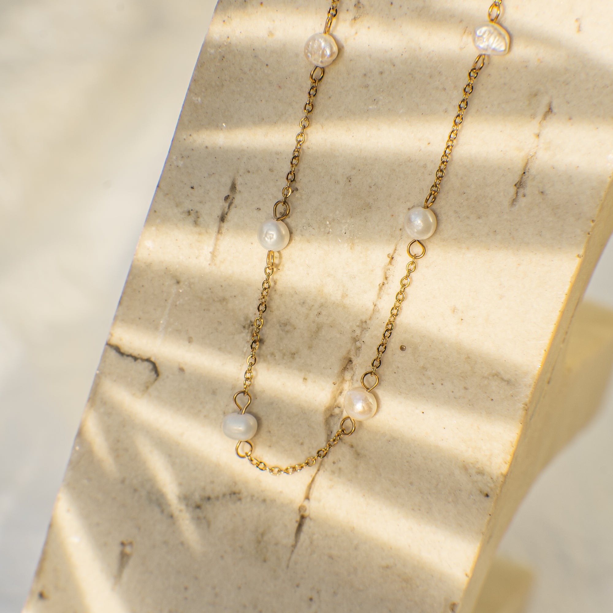 Gold necklace with pearls on a textured beige surface