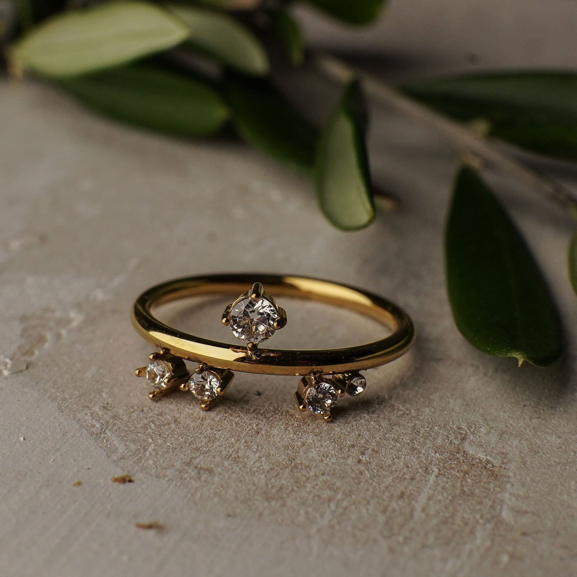 Gold ring with diamond accents on a textured surface with green leaves in the background