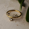 Gold ring with three diamond-like stones on a textured surface with green leaves.