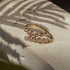 A gold ring with twisted zirconia bands and sparkling gems set in a ring, placed on a textured surface with a shadow falling over it.