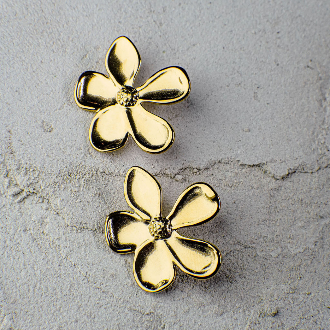 Gold flower-shaped earrings on a textured gray surface