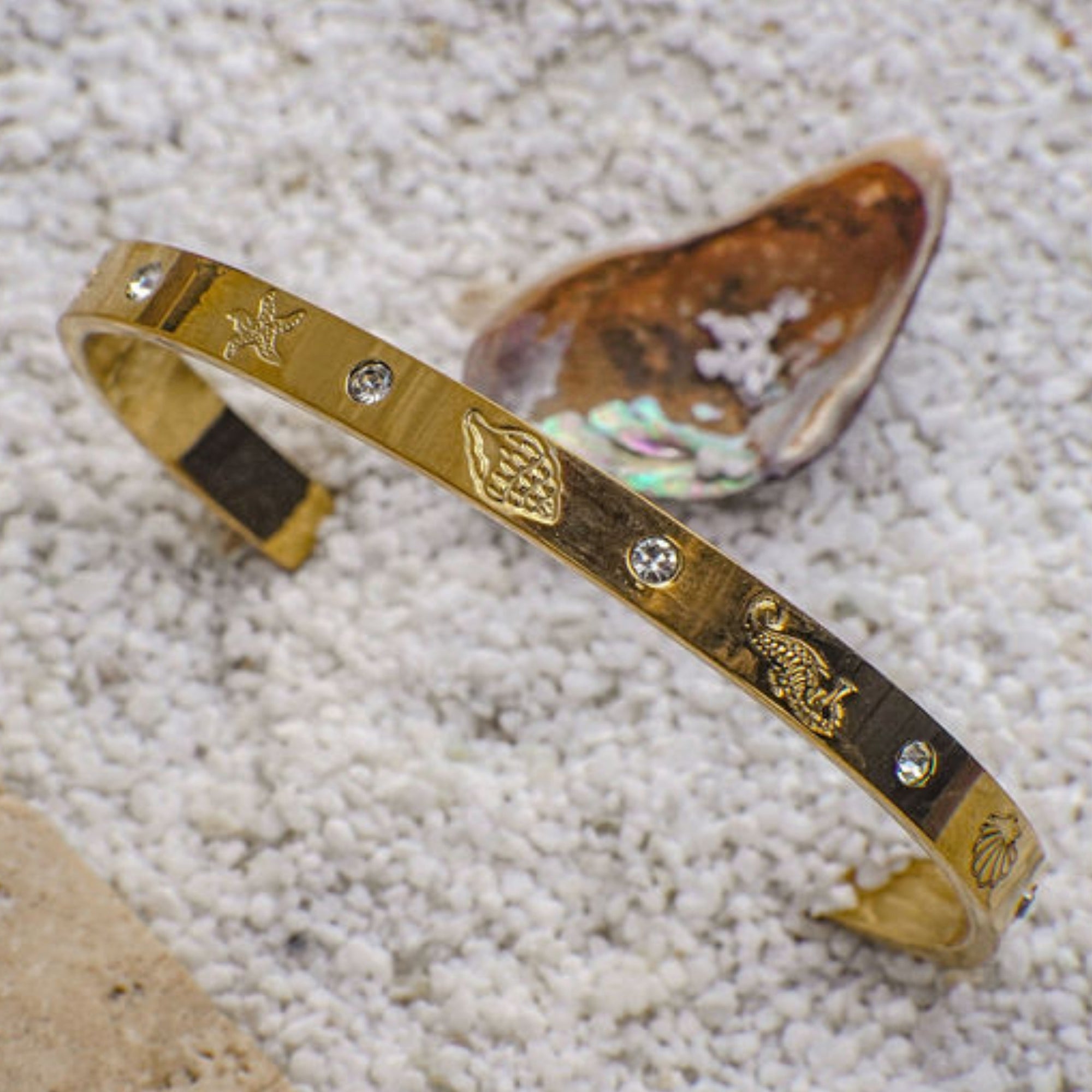 Gold bracelet with engraved designs on a sandy background