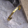 Gold bracelet with engraved designs and gemstones on a textured stone surface