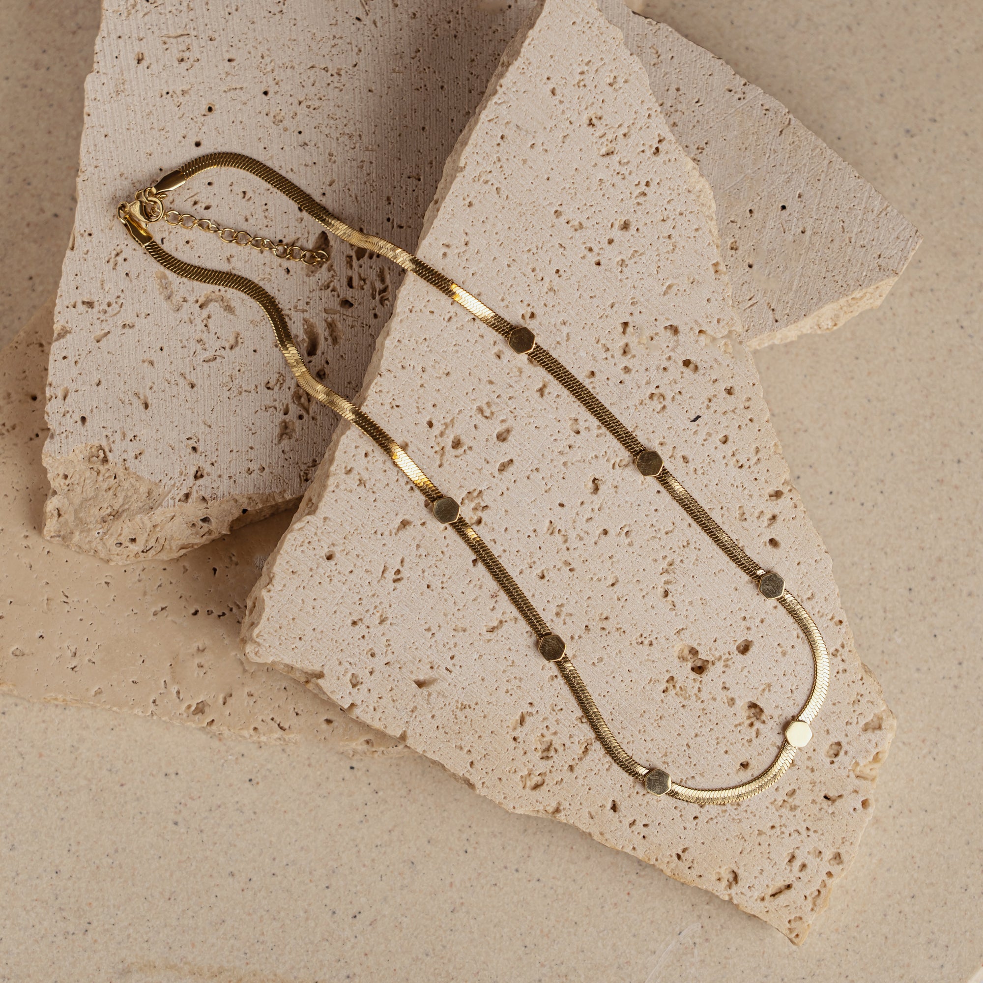 A gold-colored necklace with round beads laid out on a textured surface.