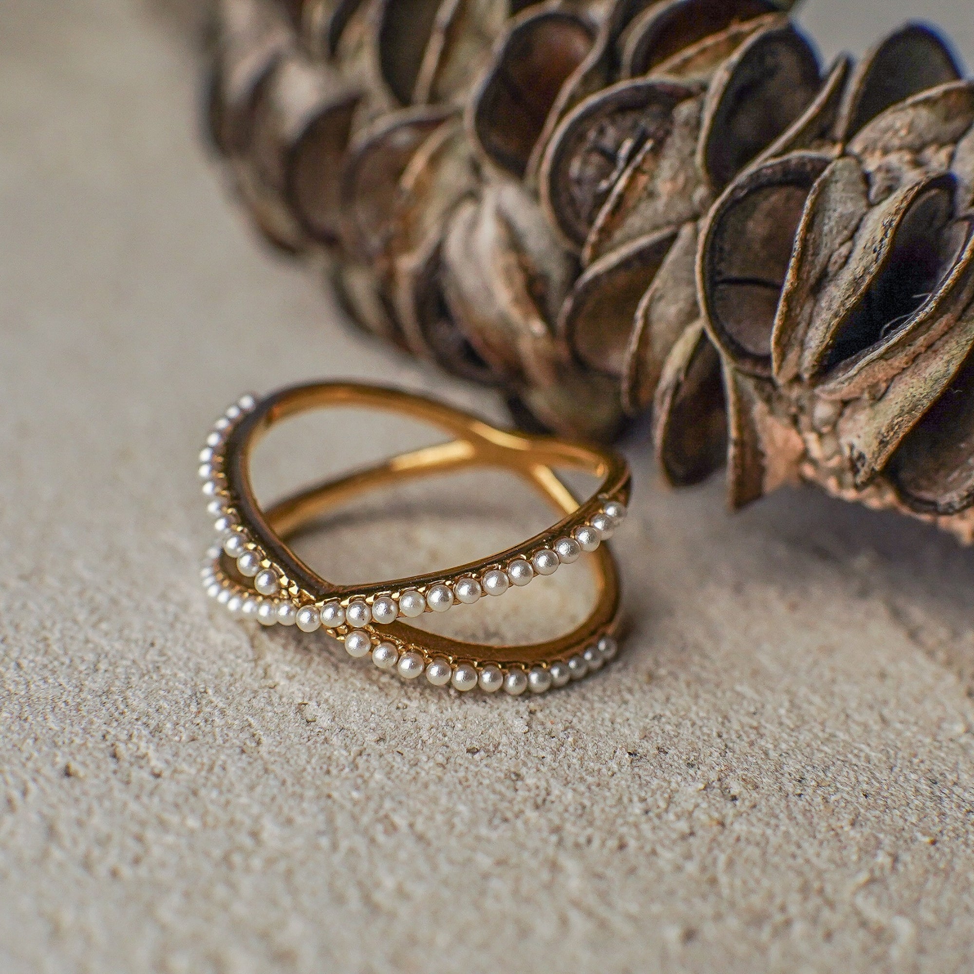 Gold ring with pearl accents on a textured surface next to a dried plant.