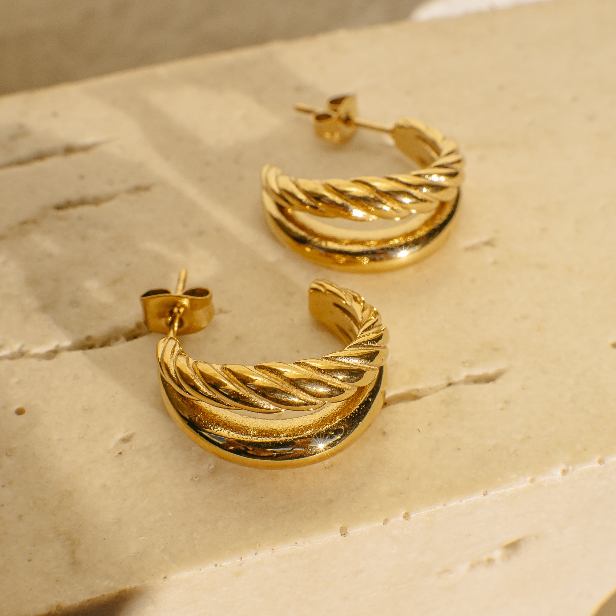 Gold hoop earrings on a textured beige surface