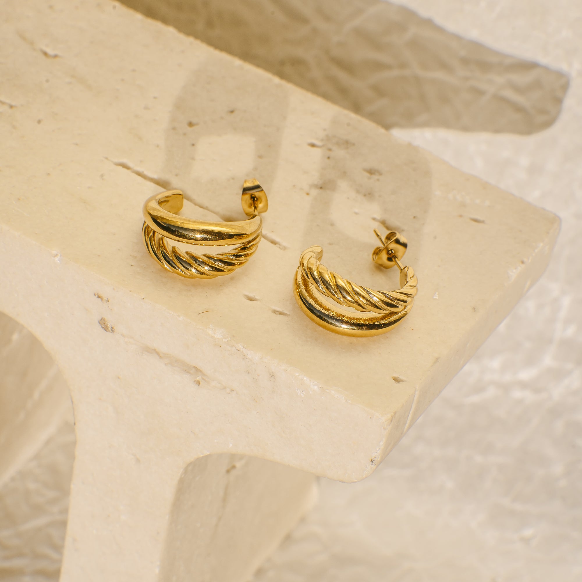 Gold hoop earrings on a textured beige surface