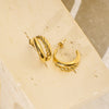 Gold hoop earrings on a beige stone surface