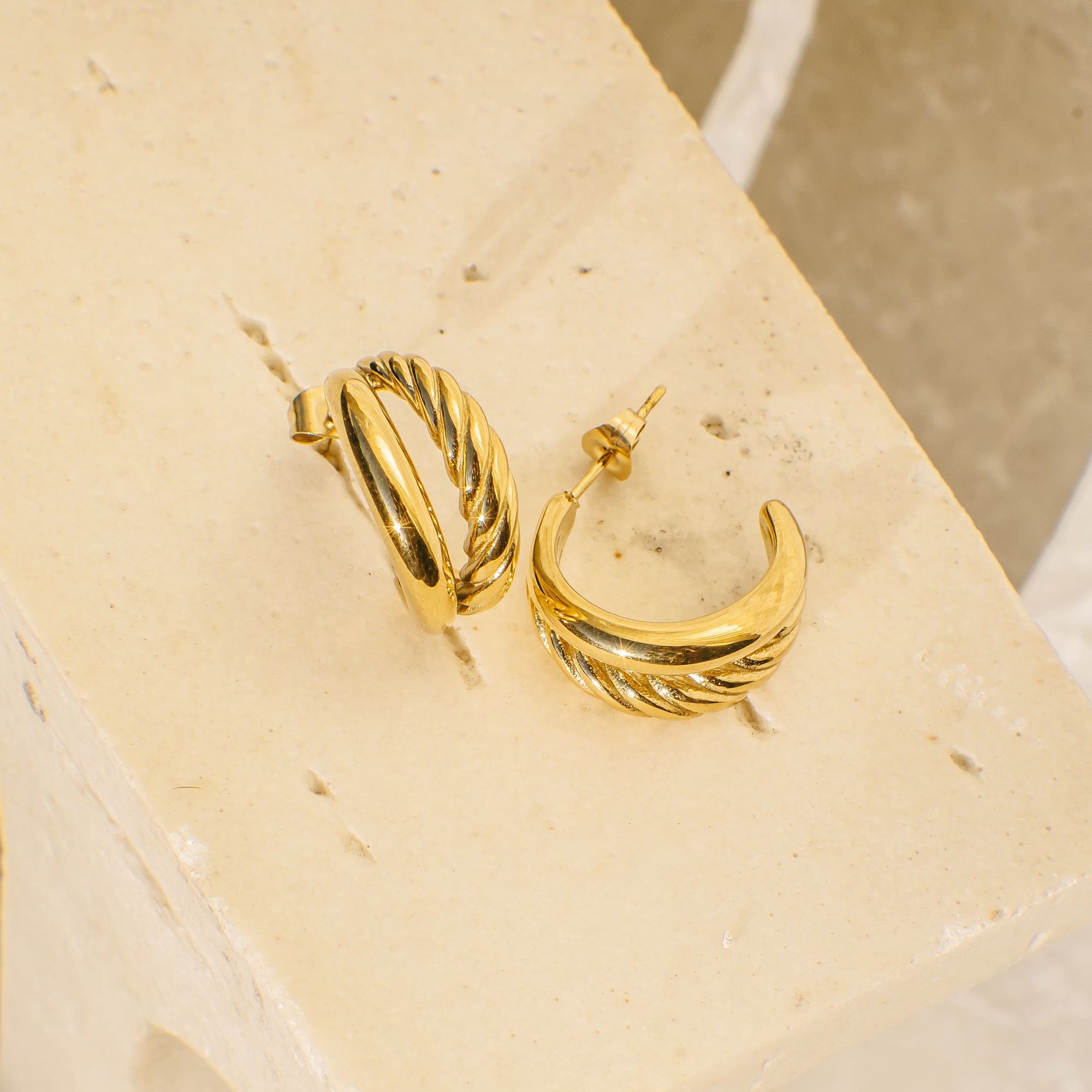 Gold hoop earrings on a beige stone surface