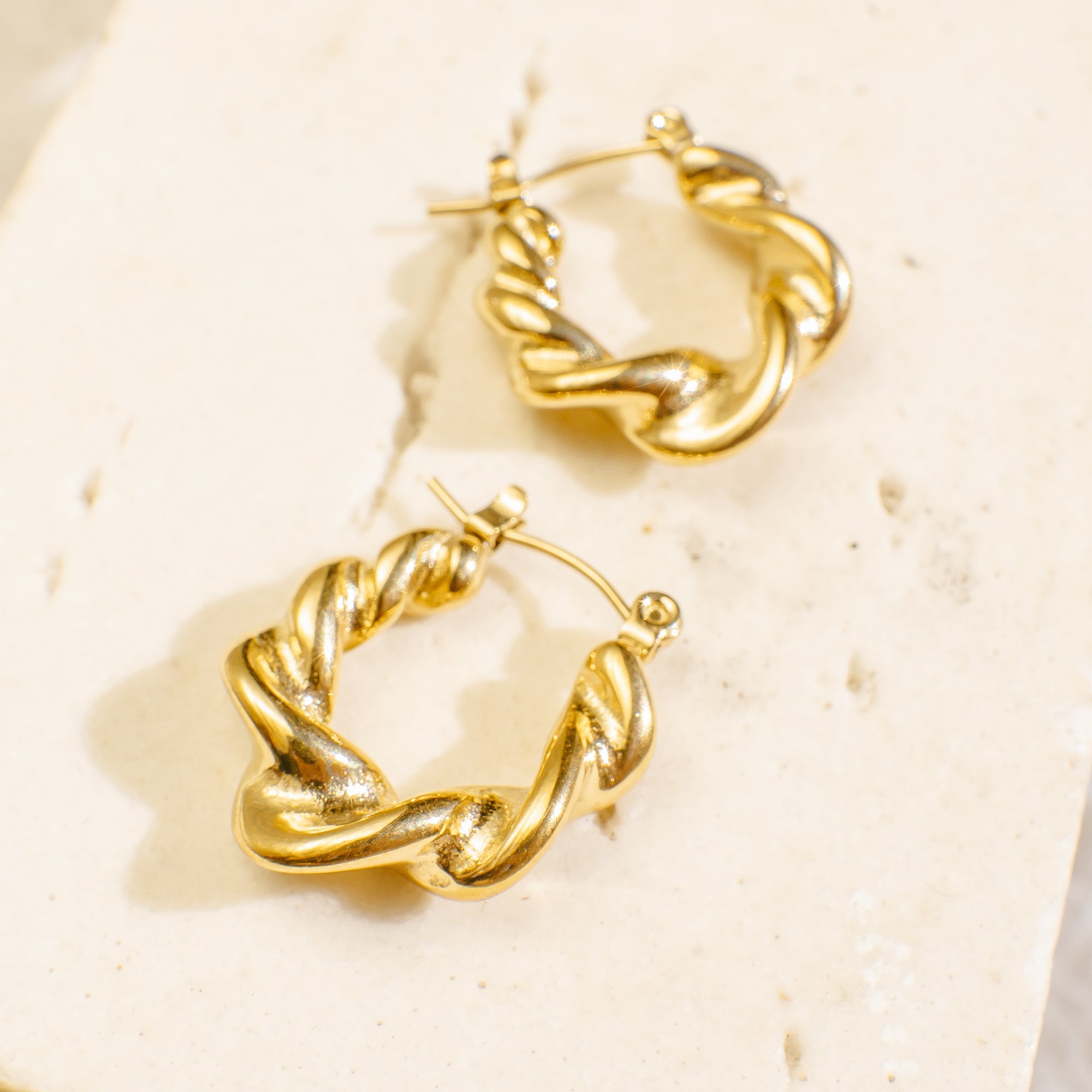 Gold hoop earrings on a textured beige surface