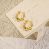 Gold hoop earrings on a beige stone surface