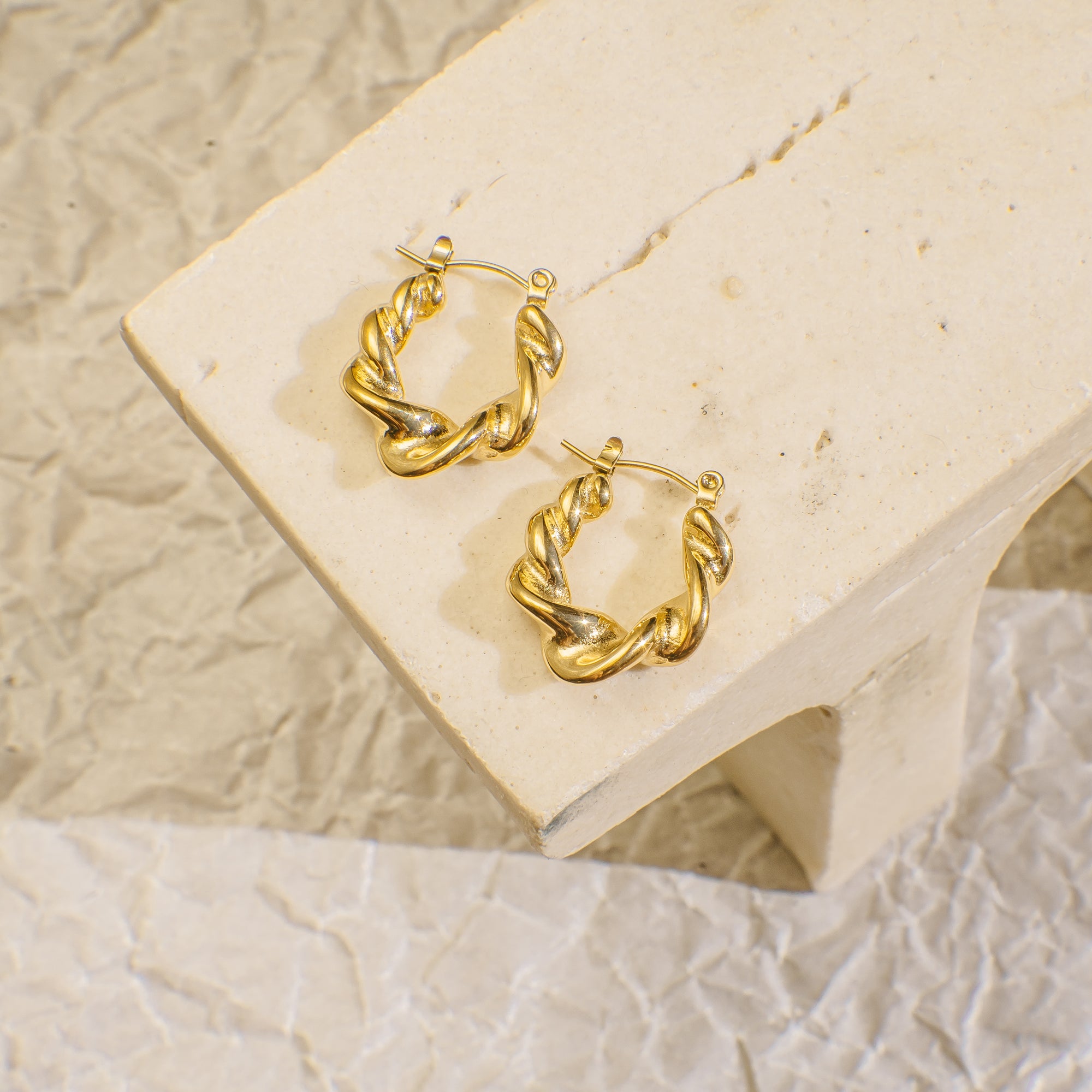 Gold hoop earrings on a beige stone surface