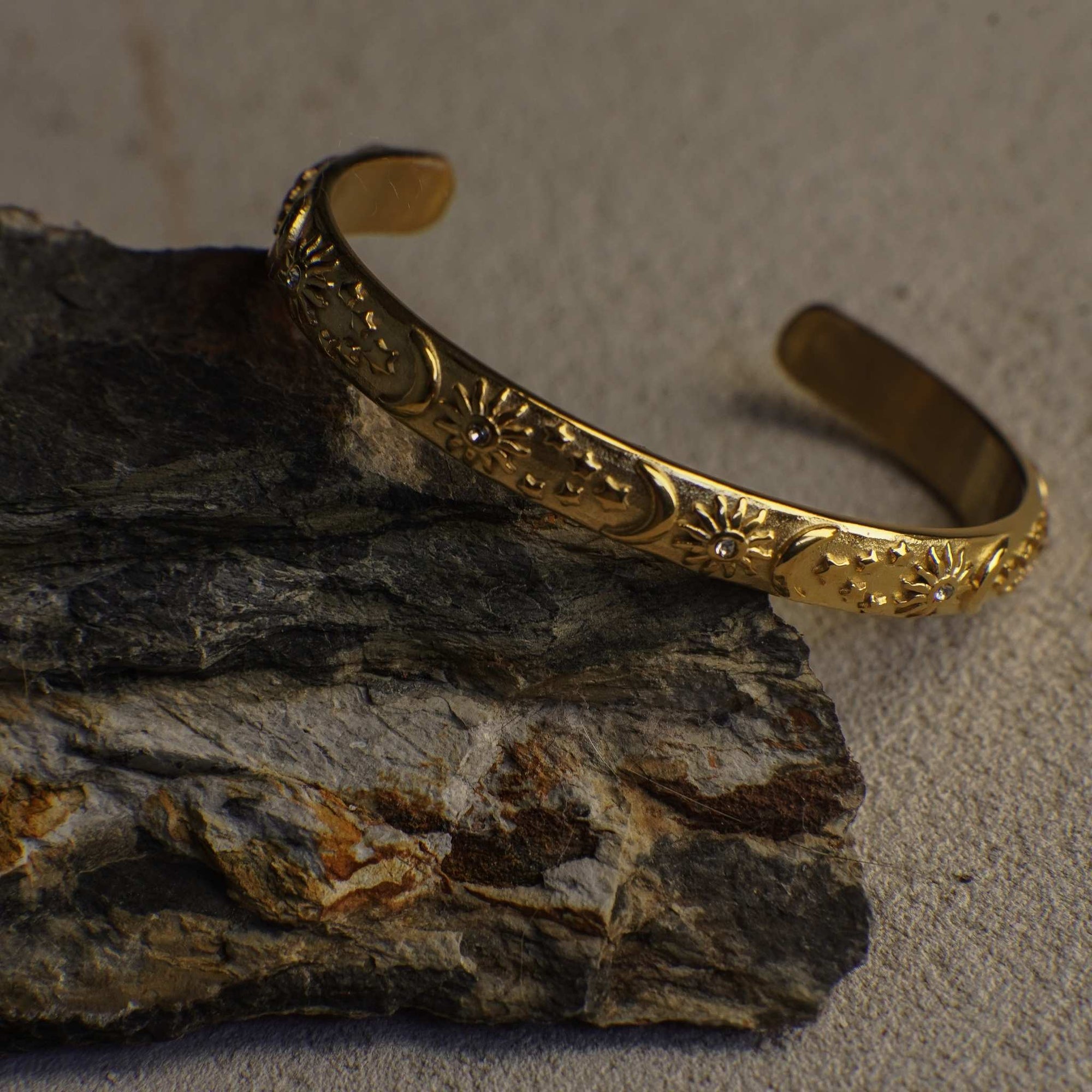 Gold bracelet with intricate designs on a stone surface