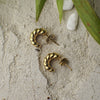 Gold hoop earrings on a textured surface with leaves and stones in the background