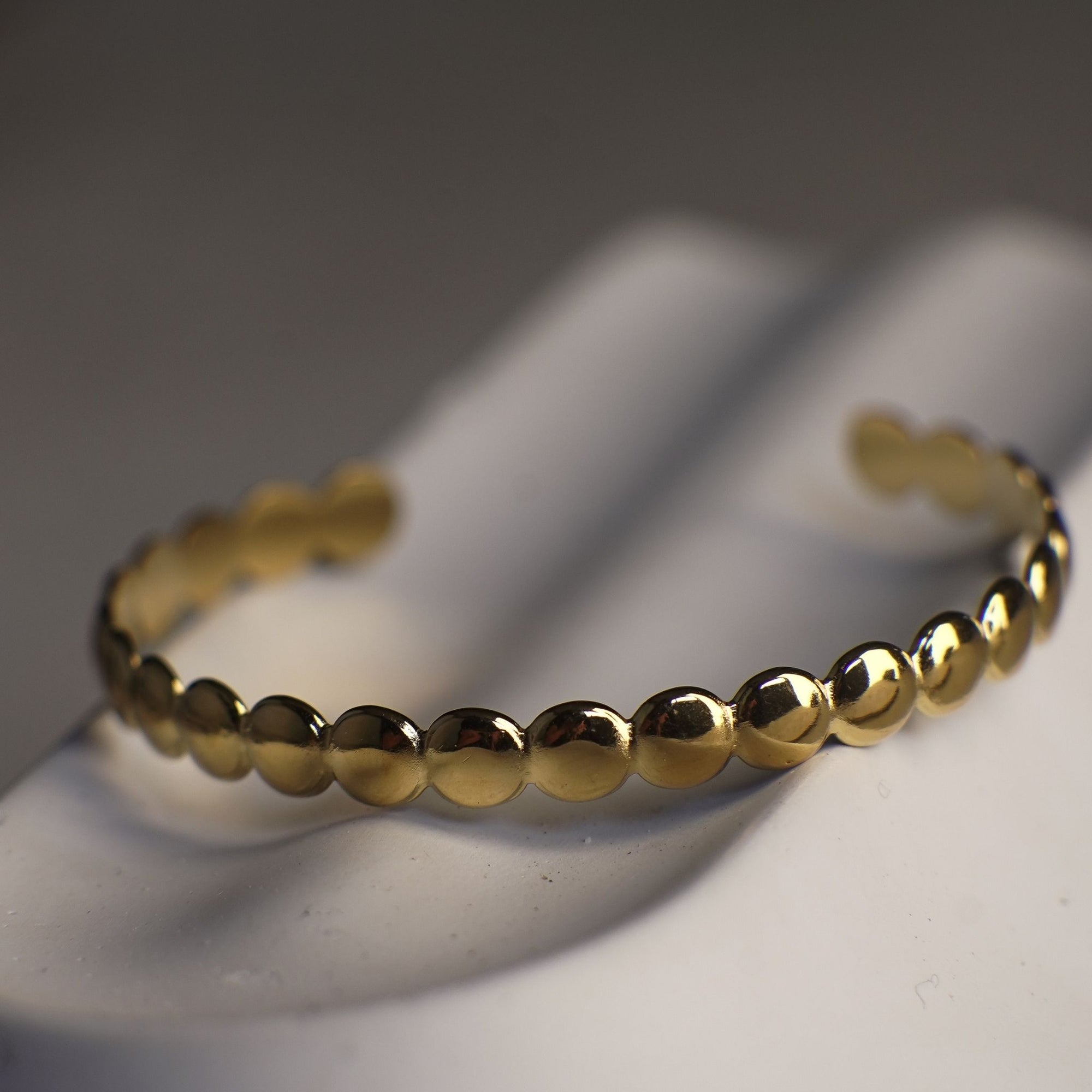 Gold beaded bracelet on a white surface with a dark background